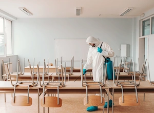 man sterile uniform with gloves mask holding sprayer spraying with disinfectant floor classroom 1